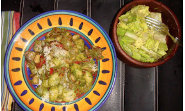 Gold and navy pasta bowl filled with gnocchi covered with pesto sauce and a wood salad bowl filled with Caesar Salad