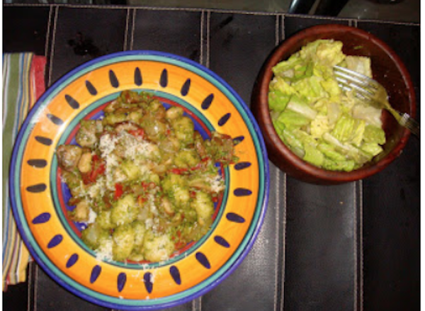 Gold and navy pasta bowl filled with gnocchi covered with pesto sauce and a wood salad bowl filled with Caesar Salad