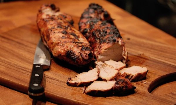 Two whole balsamic glazed pork tenderloins with pork slices & knife on wood cutting board