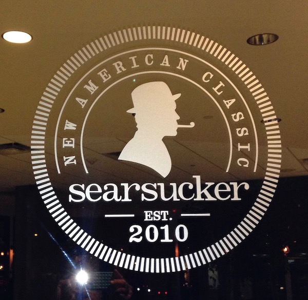 A glass door that is etched with a silhouette of a man with a hat smoking a pipe and Searsucker 2010.
