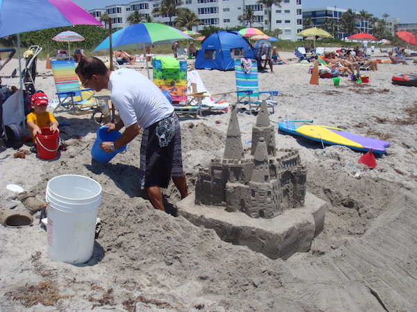 A man creating a moat around a sand castle on the beach