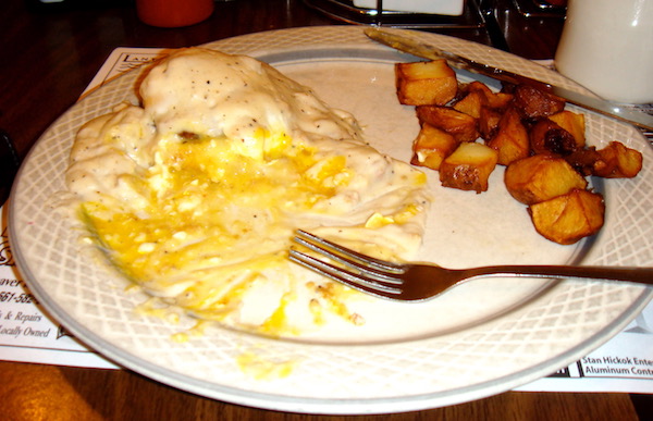 White plate with eggs, creamy sauce and hash brown potatoes and a fork.