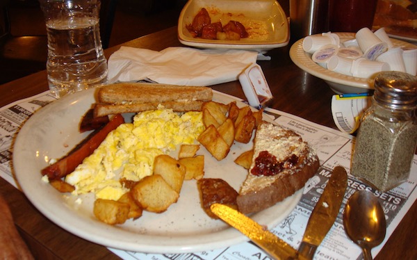 A white plate topped with toast, scrambled eggs hash browns and a triangle of buttered toast with jam.