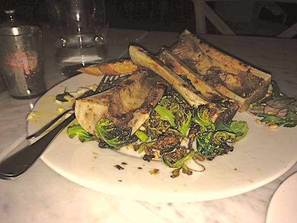 A white plate mounded high with empty roasted marrow bones and greens