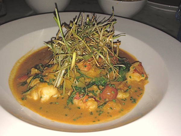 A shallow white bowl filled with sauce, gnocchi, lobster and greens