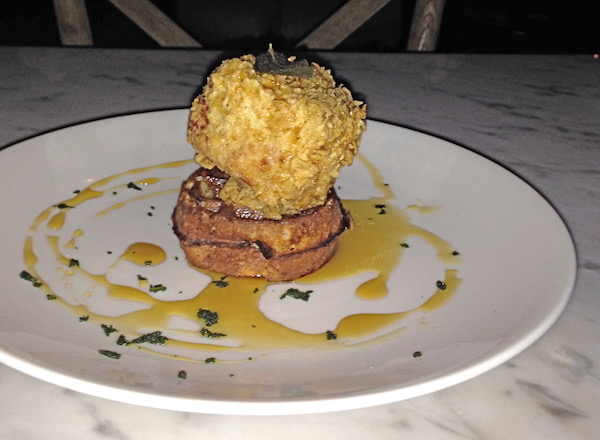 A white plate topped with a waffle and a cube of food that is battered and fried and honey on the plate.