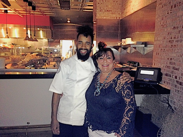 A chef in a chef coat and a woman in a lace top in front of an open kitchen