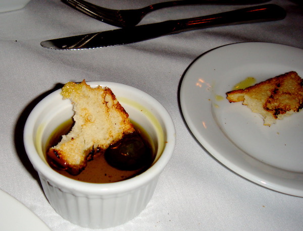 A white plate and a white ramekin on a white tablecloth holding a piece of focaccia and olive oil.