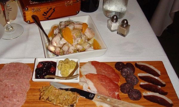 A large charcuterie board with cured meats, condiments and a bowl of seafood salad.