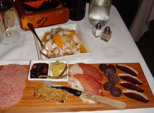 A large charcuterie board with cured meats, condiments and a bowl of seafood salad.