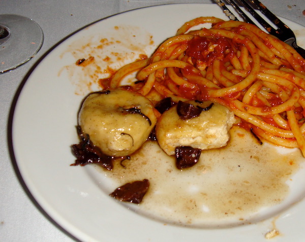 A white dinner plate with Gnudi with Shiitake Mushrooms and Buccatini all'Amatricianna on a white tablecloth.