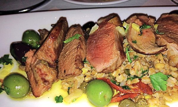 A large white oval plate covered with New Mexican Lamb with Faro and Olives