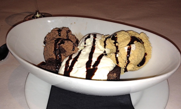 A white oval bowl filled with three scoops of ice cream and dried with fudge sauce and fresh whipped cream.