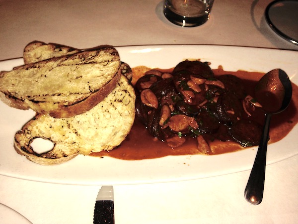A white plate filled with a saucy entrée and two slices of garlic bread.
