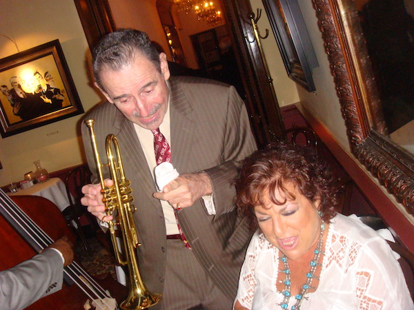 Man in brown suit with trumpet next to woman in white blouse singing