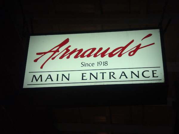 White lit sign on black background with Arnaud's in red and rest of writing Since 1918 Main Entrance in black