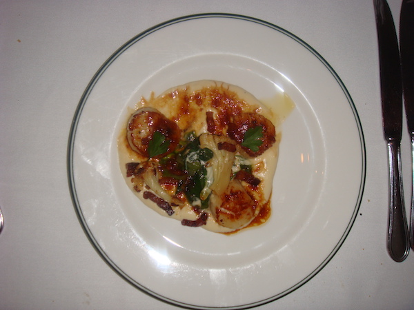White plate with thin black rim holding 3 seared scallops with sauce and vegetables