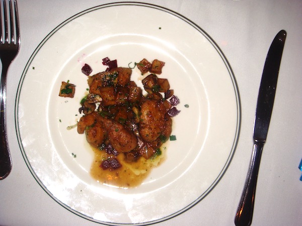 White plate with sweetbreads, mustard sauce and vegetables strewn on plate sitting on a white tablecloth