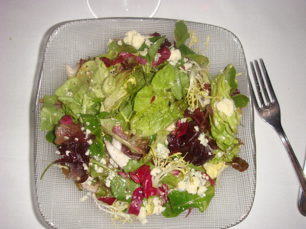 Square glass plate piled high with Bayona Salad of Mixed Field Greens with Balsamic Vinaigrette and Great Hill Blue Cheese