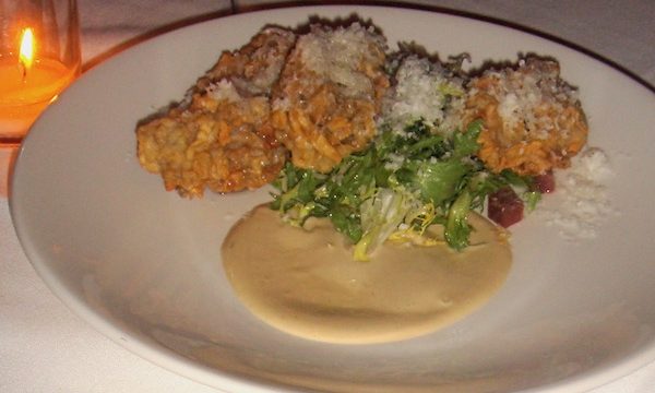 A white dinner plate topped with fried oysters, greens, ham and sauce
