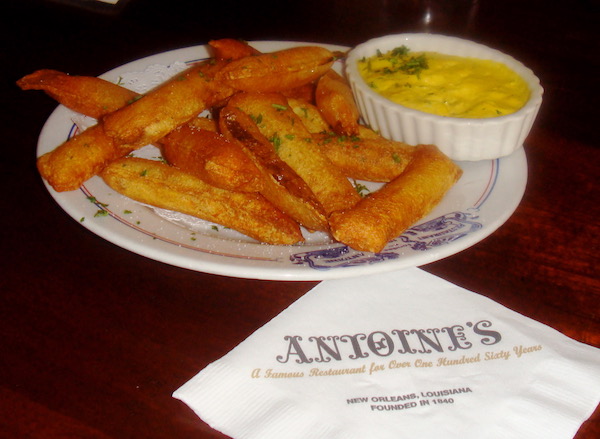 A large plate of soufflé potatoes with a dish of bearnaise sauce and a napkin the says Antoine's