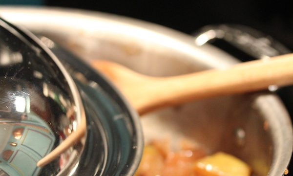 A stainless steel pan filled with apple compote and a wooden spoon with the lid partially covering pan
