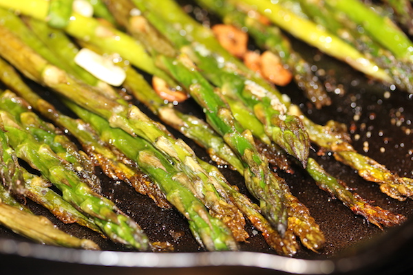 Sauté pan filled with thin asparagus spears and slices of garlic