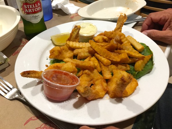A white plate with a pile of fried shrimp and a small dish of cocktail sauce