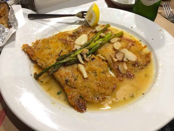 A large piece of battered snapper on a white plate with sauce and lemon wedge