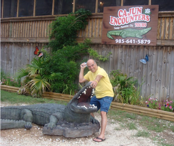 Man in yellow shirt and olive green shorts petting a large alligator sculpture