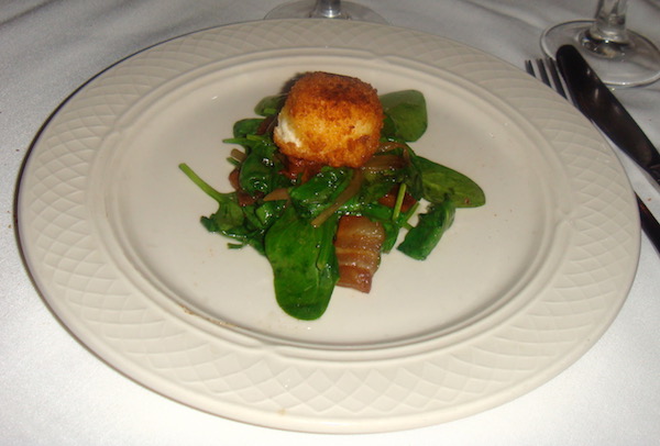 Ivory plate filled with spinach, bacon and a golden brown bread crumb crusted medallion of goat cheese