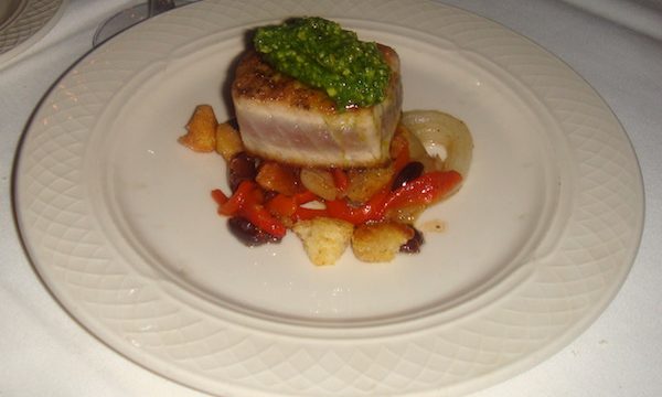 Ivory dinner plate with colorful vegetables topped by a rectangle of seared tuna that is sauced with a verdant green arugula pesto