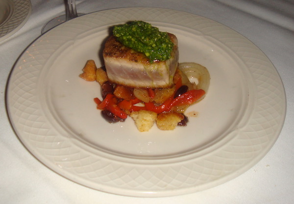 Ivory dinner plate with colorful vegetables topped by a rectangle of seared tuna that is sauced with a verdant green arugula pesto