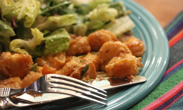 An aqua dinner plate filled with small fried shrimp and salad greens with a creamy dressing. A knife and fork are resting on the front of the plate