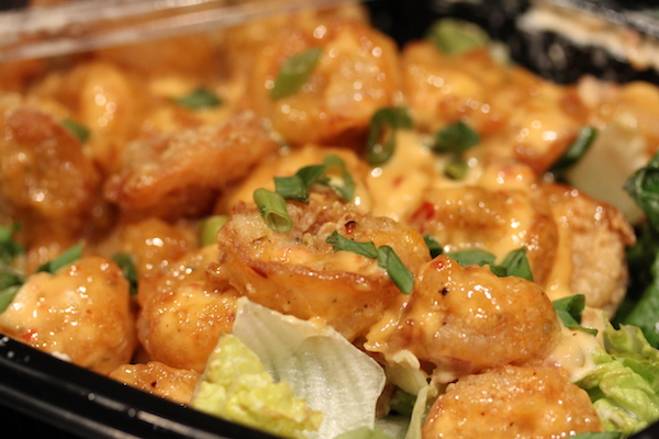 A black take-out box filled with fried shrimp with a creamy pink dressing sitting on a bed of lettuce