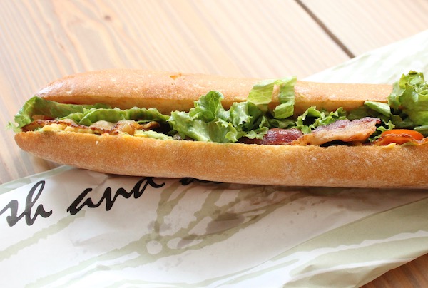 A long baguette bread filled with meats, lettuce and cheese sitting on white deli paper