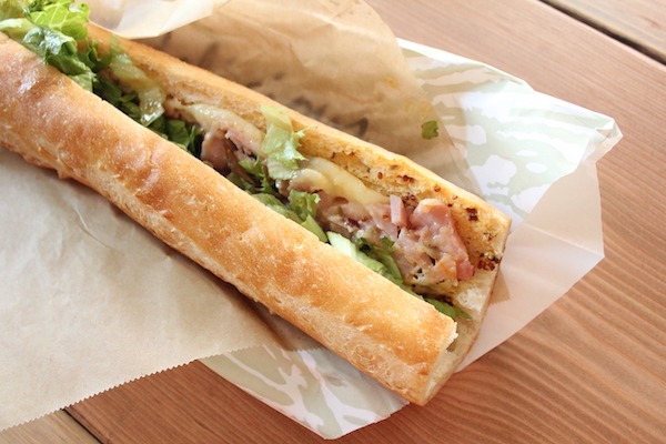 A long baguette bread filled with meats, lettuce and cheese sitting on white deli paper