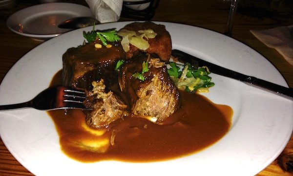 A white dinner plate topped with Braised Beef Short Ribs and lots of gravy