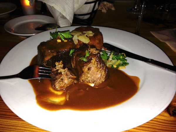 A white dinner plate topped with Braised Beef Short Ribs and lots of gravy