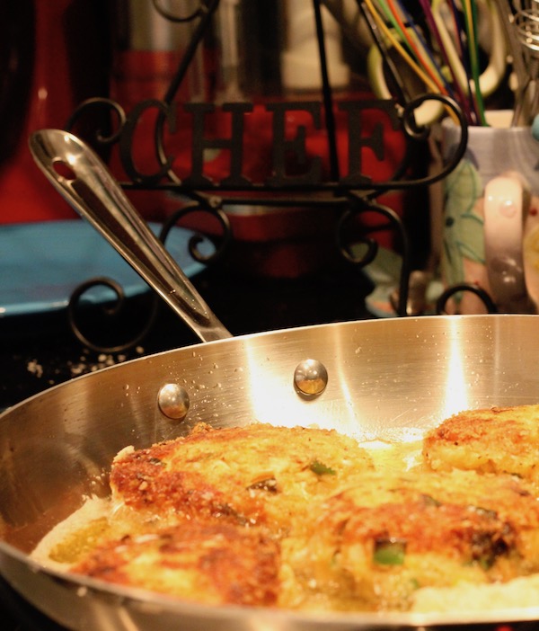 A sauté pan with Golden Brown Red Pepper Crab Cakes Frying and utensils in the background