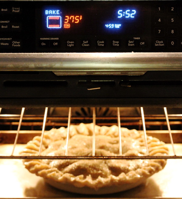 A double crust pie on a sheet pan in an oven with temperature showing 375F