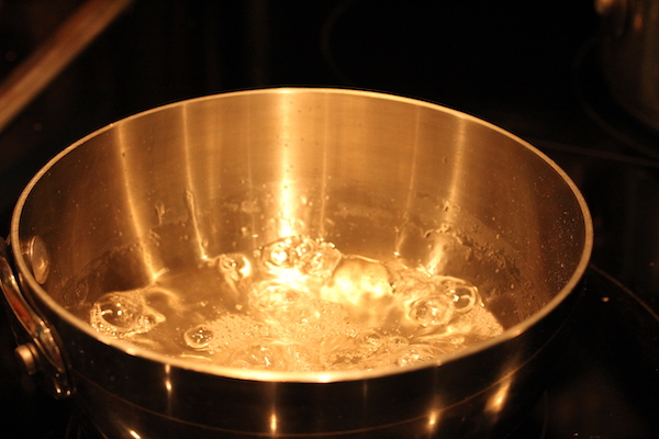 Two sauce pans on a glass topped stove. One of the pans has sugar heating for caramel.