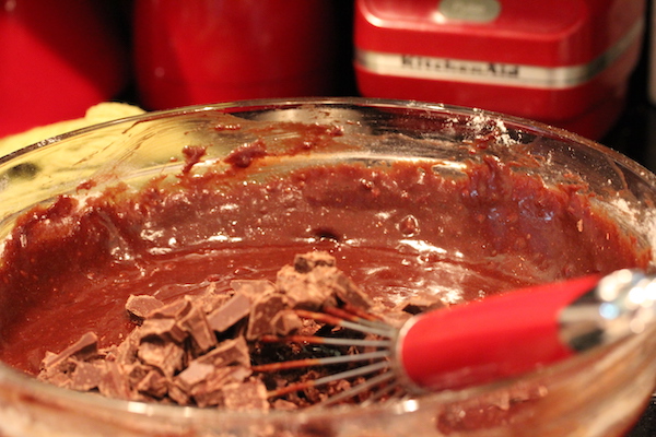 A large glass bowl filled with fudgy batter being stirred by a red handled whisk.