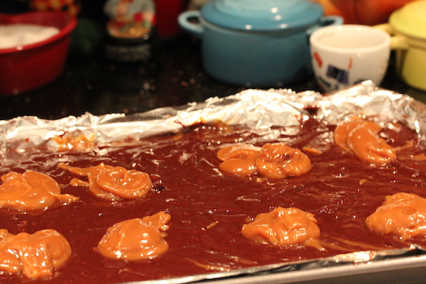 A foil lined pan filled with brownie batter with large dollops of peanut butter caramel on top.