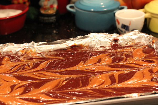 A foil lined pan with swirled brownie and peanut butter caramel batters.