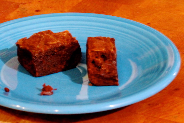 A small turquoise plate topped with two squares of chocolate brownies. Plate is sitting on a butcher block.