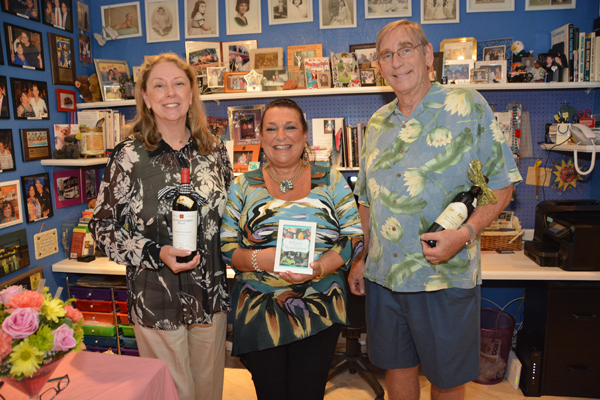 A woman holding a bottle of wine, a woman holding a book and a man with a bottle of wine.