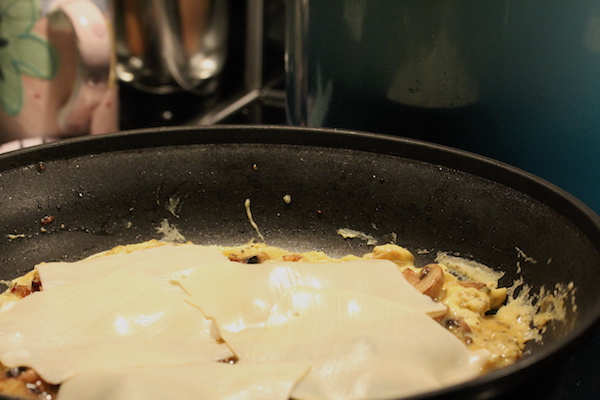 An anodized pan filled with cooked eggs and onions and covered with melted pale yellow cheese