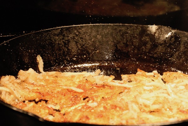 A cast iron pan with shredded potatoes turning golden brown.
