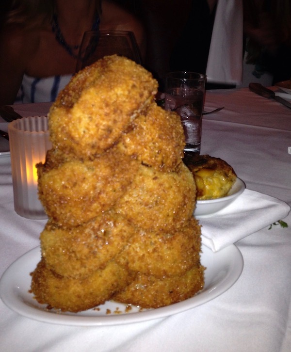 A tower of thick sliced and fried onion rings sitting on a white tablecloth